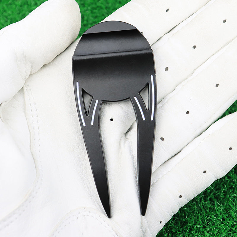 Black golf divot tool on a white golf glove with green grass in the background